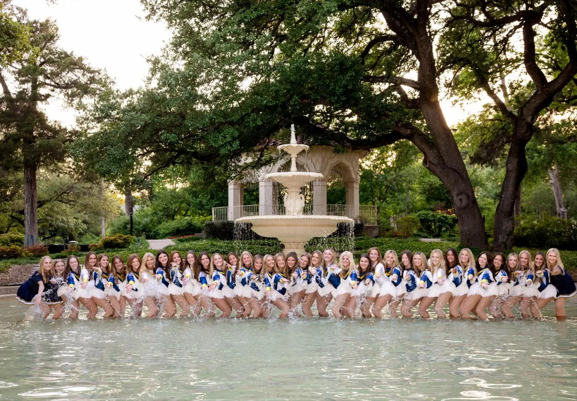 Highland Park Belles seniors in a kick line splashing in a fountain in their blue, white, and gold uniforms